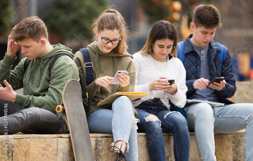 Four teenagers chatting on their smartphone on walking
