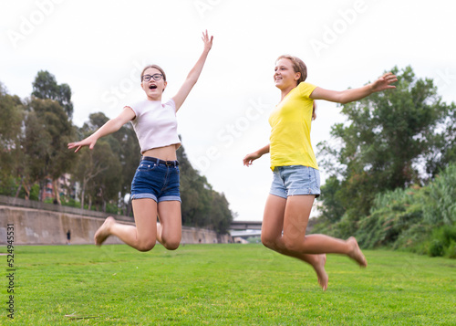 Portrait of cheerful teenage girls jumping together in summer city park. Concept of happy adolescence