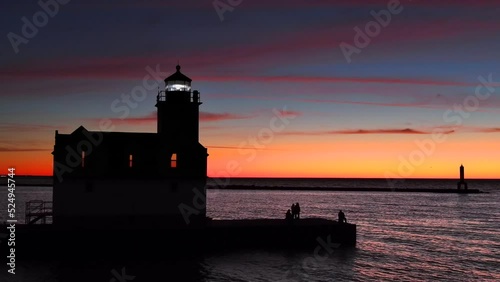 Incredible, colorful sunrise sky over lighthouse, silhouetted people fishing.
 photo