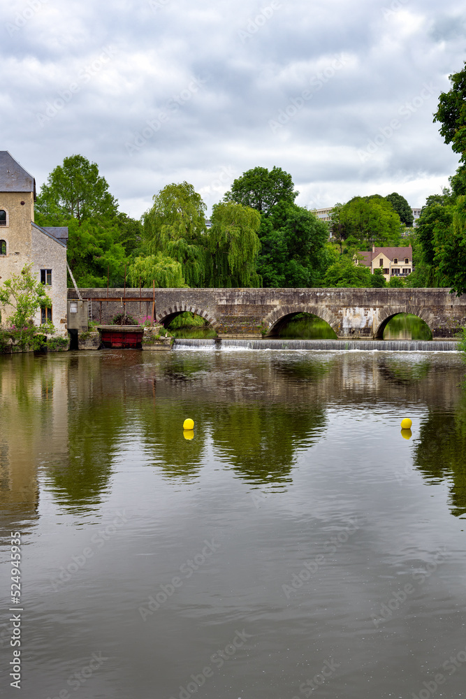 View of the Sillé bridge and the Creusot grain water mill over the river Sarthe on a cloudy spring day, Fresnay-sur-Sarthe, France View of the Sillé bridge and the Creusot grain water mill over the river Sarthe on a cloudy spring day, Fresnay-sur-Sarthe, France
