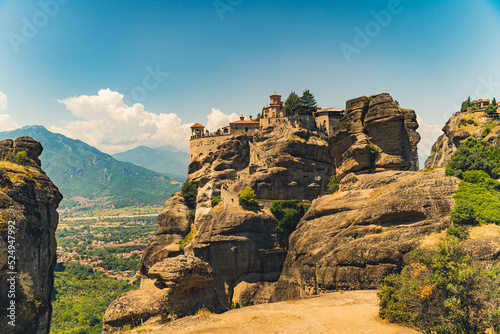 Impressive orthodox mountain monasteries. Beautiful view of one side of Meteora Monastery built on high rock formation. Blue sky. Greek city in the background. High quality photo