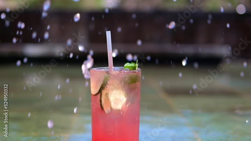 An ice cube is dipped into a glass with watermelon katel with cucumber slices and mint leaves, which are sprinkled with cold drops of a refreshing drink. Cold cocktail. Nice slow motion video. photo