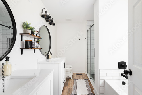 Fotografia, Obraz A modern farmhouse bathroom with a white vanity and marble countertop, circular black mirrors, and a view to the white subway tile shower