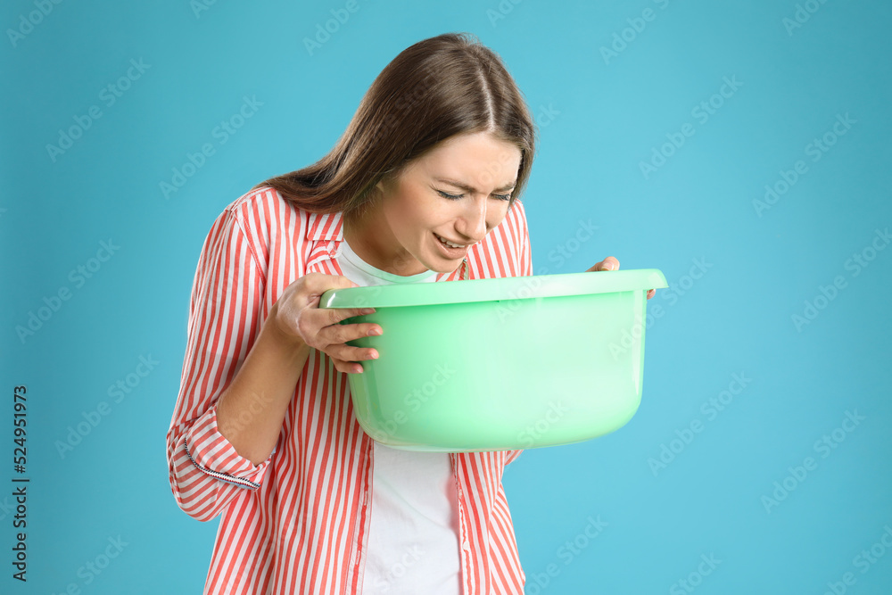Woman with basin suffering from nausea on light blue background. Food poisoning