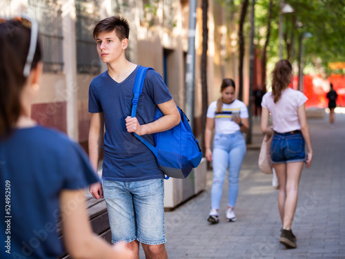 Confident teen boy with backpack strolling through modern city streets on sunny summer day