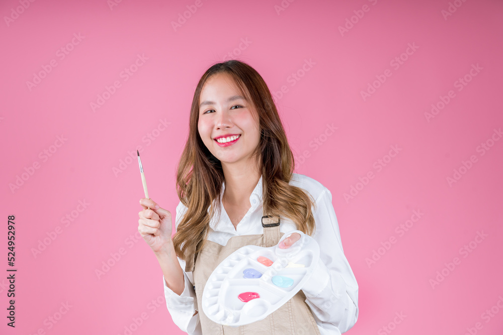 Beautiful Asian woman painter artist holding quill pen and color palette using paintbrush for desigh, drawing, paint workshop on pink background Beautiful Asian woman painter artist holding quill pen and color palette using paintbrush for desigh, drawing, paint workshop on pink background