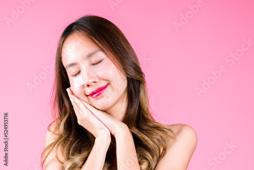 Beauty attractive young asian woman applying eye tretment rejuvenation on her under eyes, facial skin care makeup on the pink background