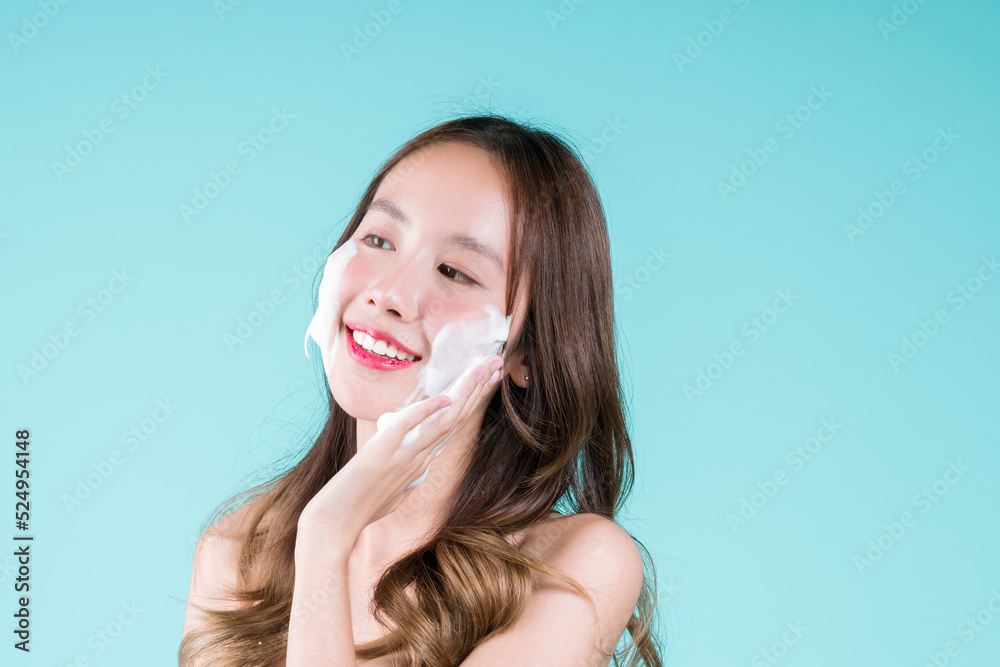 Wash and scrub on face of Happy charming Asian woman applying facial foam cleanser on her face on the blue background.