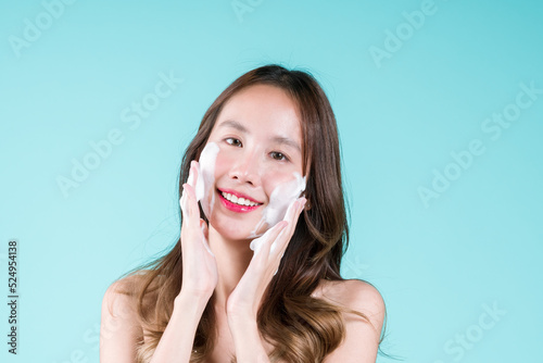 Facial foam cleanser wash and scrub, Happy charming young Asian woman applying on her face on the blue background.