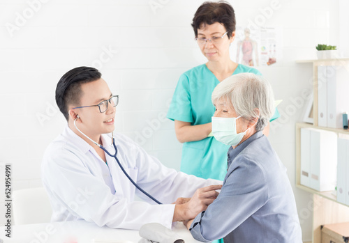 Asian doctor talk with old female patient about disease symptom, he use stethoscope listening on chest of patient, elderly health check up