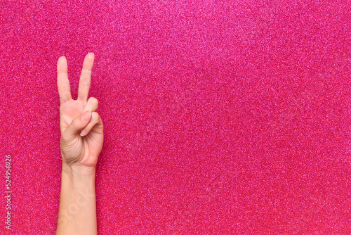 woman hands making peace and victory symbol on glitter pink background