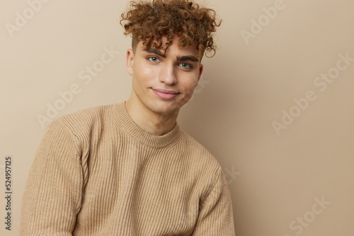 a charming man in a beige sweater stands on a beige background with a hat on his head and looks pleasantly into the camera
