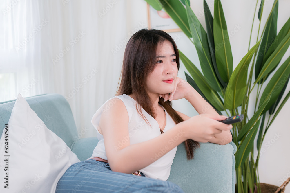 Asian woman use remote control for watching tv her enjoy and fun sitting near sofa in living room at home Asian woman use remote control for watching tv her enjoy and fun sitting near sofa in living room at home