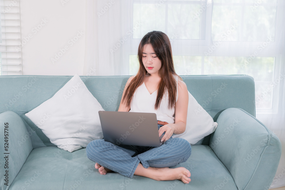 Asian woman use laptop computer her enjoy and fun sitting on sofa in living room at home Asian woman use laptop computer her enjoy and fun sitting on sofa in living room at home