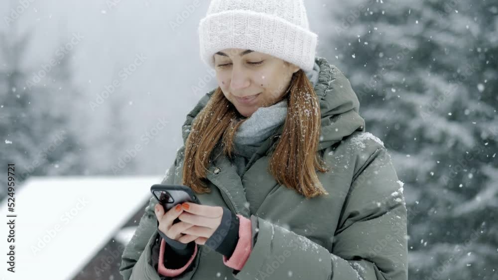 Young happy woman uses a mobile phone in winter under a snowfall, typing text, surfs the Internet Young happy woman uses a mobile phone in winter under a snowfall, typing text, surfs the Internet