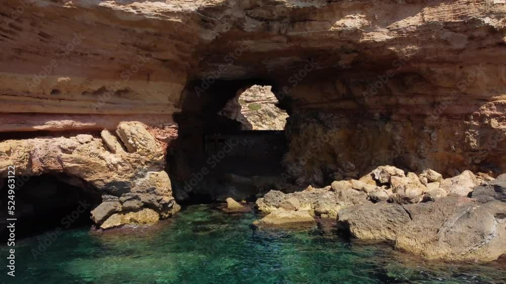 secret cave hole in mountain at bay.Unbelievable aerial view flight fly backwards drone footage of cliff edge beach Sa Figuera borda Ibiza summer 2022