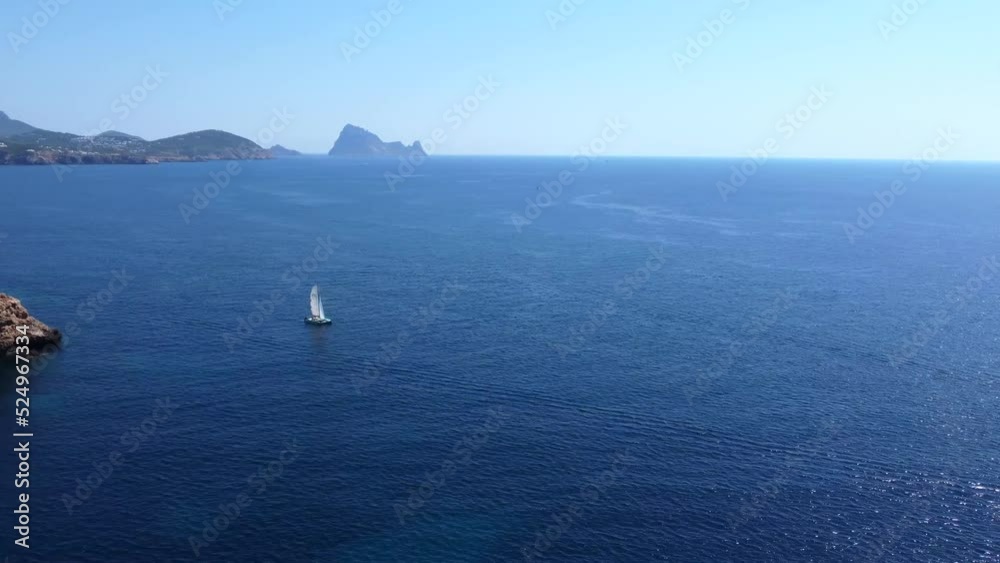 Boats in the blue bay infinite horizonCalm aerial view flight panorama curved flight drone footage at cliff edge beach Sa Figuera borda Ibiza summer 2022.