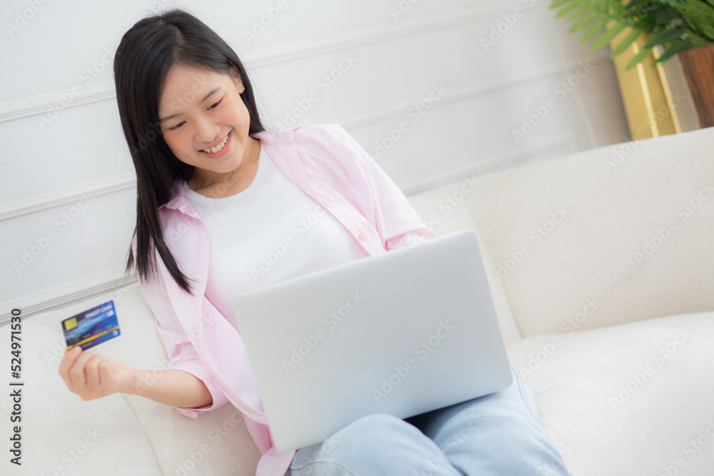 Young asian woman sitting on sofa using laptop computer online shopping with credit card, happy female payment with debit card on couch, purchase and payment, business and technology concept. Young asian woman sitting on sofa using laptop computer online shopping with credit card, happy female payment with debit card on couch, purchase and payment, business and technology concept.