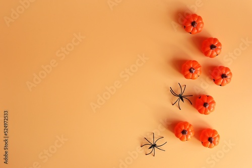  Beautiful pumpkins and two black small spider on a orange background. Creative halloween concept backdrop. 