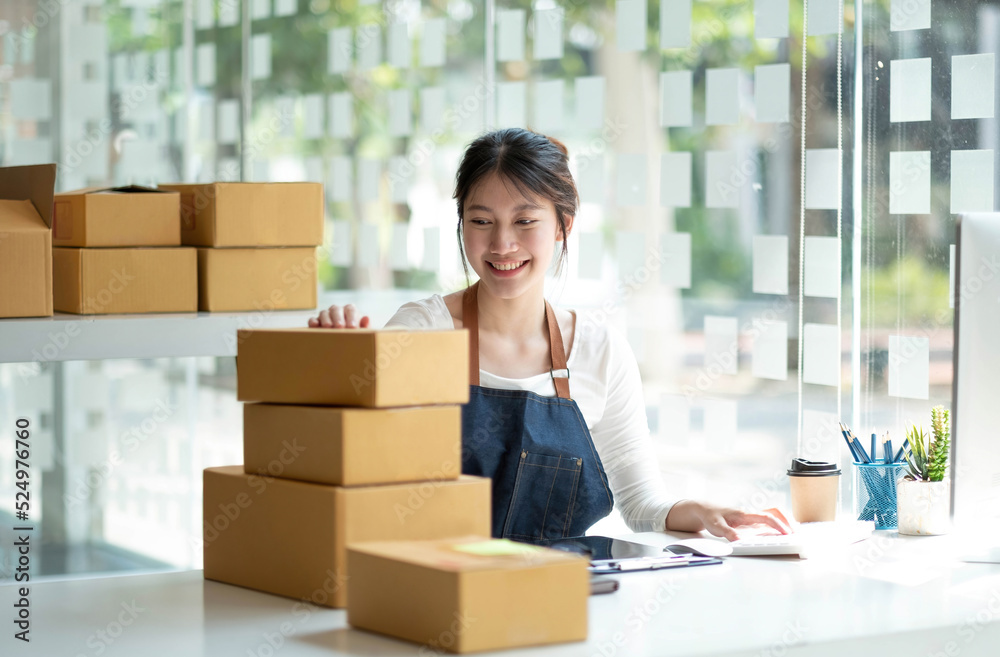 Startup SME small business entrepreneur SME or freelance Asian woman using a laptop with box, Young success Asian woman with her hand lift up, online marketing packaging box and delivery, SME concept. Startup SME small business entrepreneur SME or freelance Asian woman using a laptop with box, Young success Asian woman with her hand lift up, online marketing packaging box and delivery, SME concept.
