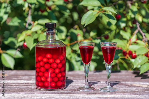 Homemade cherry brandy in glasses and in a bottle on a wooden table in a summer garden