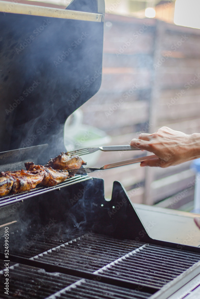 Meat on the grill. Man hand turning chicken on grill. Bardeque time on backyard. Homemade grill meat. Roasted chicken for family party. Cooking meat with smoke. Meat on the grill. Man hand turning chicken on grill. Bardeque time on backyard. Homemade grill meat. Roasted chicken for family party. Cooking meat with smoke.