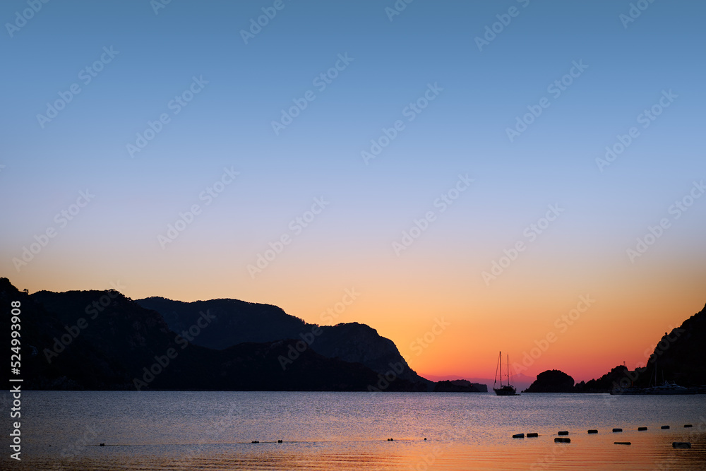 Beautiful sunrise with yacht sailing the sea with rocks islands on the background.