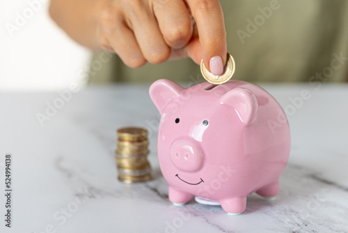 Close-up of a woman's hands putting a euro coin in a piggy bank, saving money in a crisis and inflation