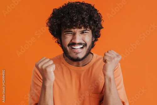 Portrait of young indian stressed curly squinting man raising fists