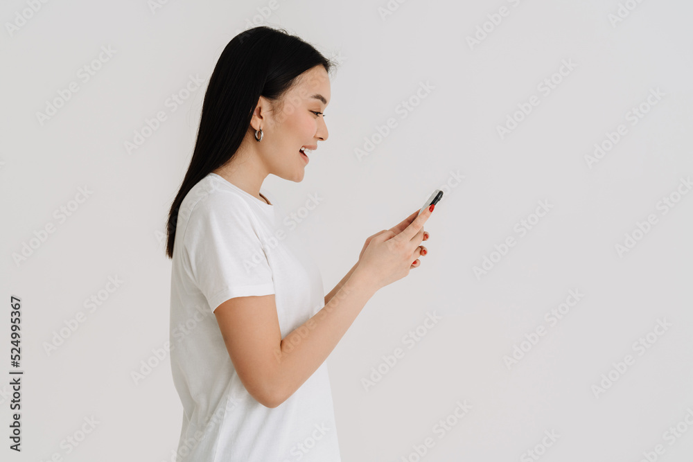 Asian excited woman wearing t-shirt smiling and using cellphone Asian excited woman wearing t-shirt smiling and using cellphone