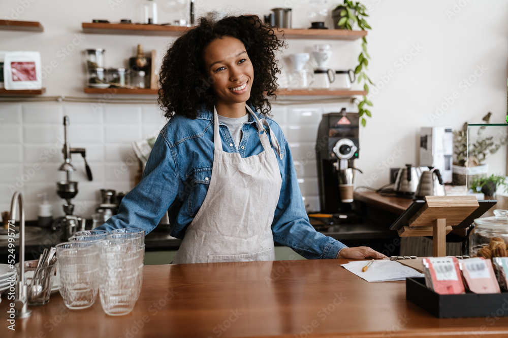 Black young barista woman wearing apron smiling while working in cafe Black young barista woman wearing apron smiling while working in cafe