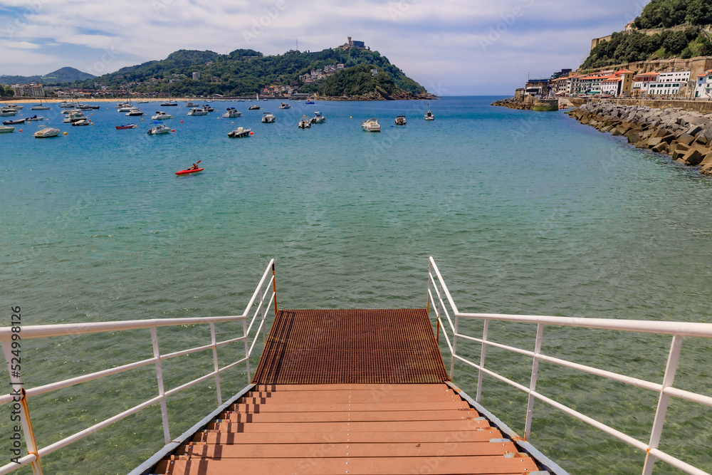 Steps leading into the water in La Concha bay with boats with Santa Clara island in the background, San Sebastian or Donostia in Basque Country, Spain