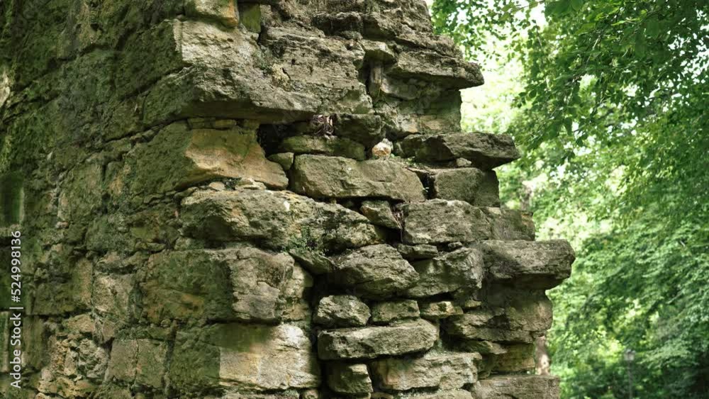 Ruin of an ancient antique stone wall of a historical building against the background of green foliage of trees. Close-up