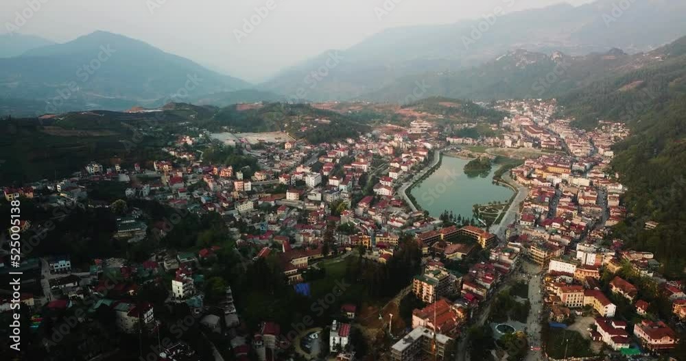 Ascending establishing aerial shot of Sapa Vietnam. An Asian town in large valley amongst foggy mountains in the background. 