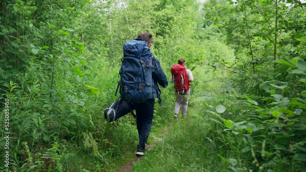 Young couple of hikers walks trying to find perfect spot for nice camping in forest. Young man and woman enjoy hiking together smiling to each other Young couple of hikers walks trying to find perfect spot for nice camping in forest. Young man and woman enjoy hiking together smiling to each other