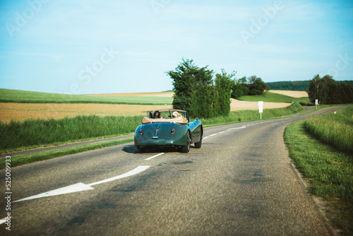 Rear view of couple inside vintage green unrecognizable car drigin on the rural road to new destiantion holiday getting away from it all