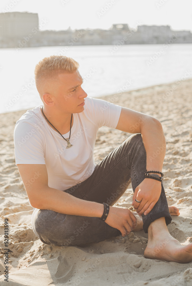Young guy at beach in tranquility mood, rest in vacation. Summer portrait of handsome men at beach, concept of vacation, rest time 