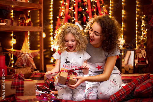 Cheerful cute curly little girl and her older sister exchanging gifts. Sisters having fun near christmas tree indoors. Loving family with presents in christmas room