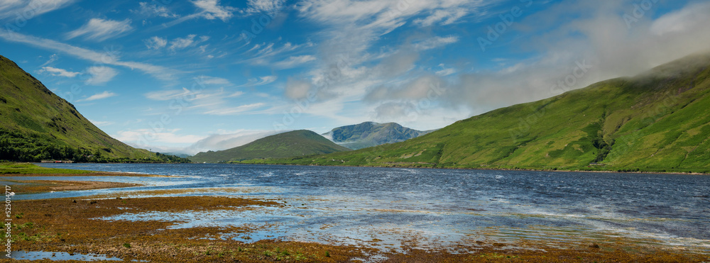 Panorama of Killary fjord in Connemara Ireland. Warm sunny day, blue cloudy sky and rich green color of mountains. Irish landscape. Popular travel area with stunning nature scenery. Nobody.