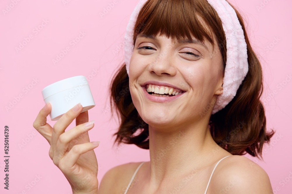 a happy, joyful, young woman stands squinting her eyes from a smile and holds a round, white jar of cream in her hand a happy, joyful, young woman stands squinting her eyes from a smile and holds a round, white jar of cream in her hand
