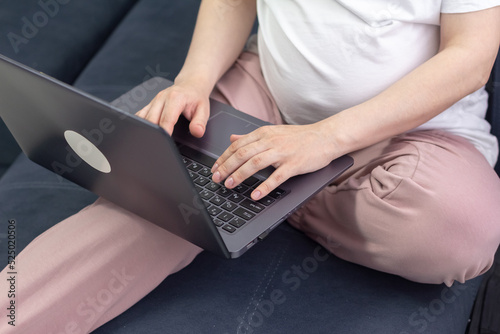 Pregnant woman in white clothes sitting and using laptop in sofa. Baby expectation. Homely atmosphere.