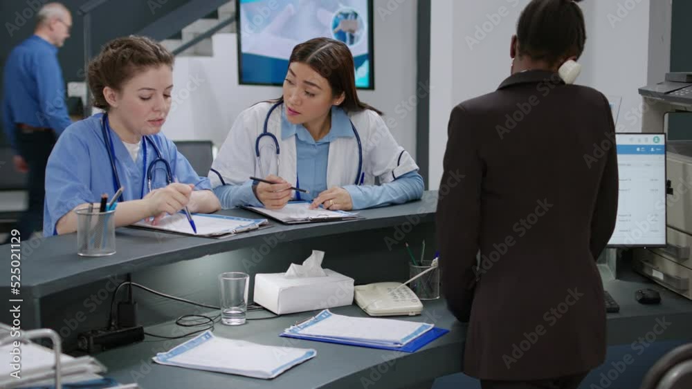Diverse medical team talking about healthcare insurance with report forms at reception counter. Nurse, doctor and receptionist helping patients with checkup appointments, hospital lobby. Diverse medical team talking about healthcare insurance with report forms at reception counter. Nurse, doctor and receptionist helping patients with checkup appointments, hospital lobby.