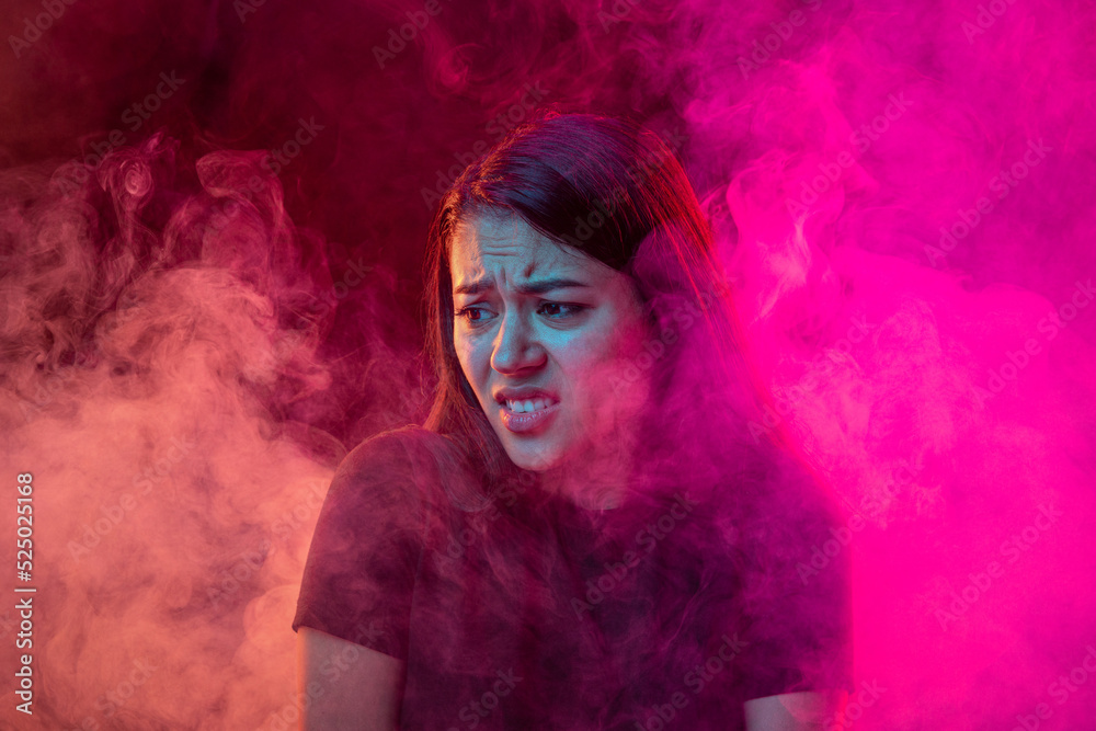 Childhood fear. Scared young dark hair woman with different emotions isolated over pink background with clouds of smoke. Concept of mental health