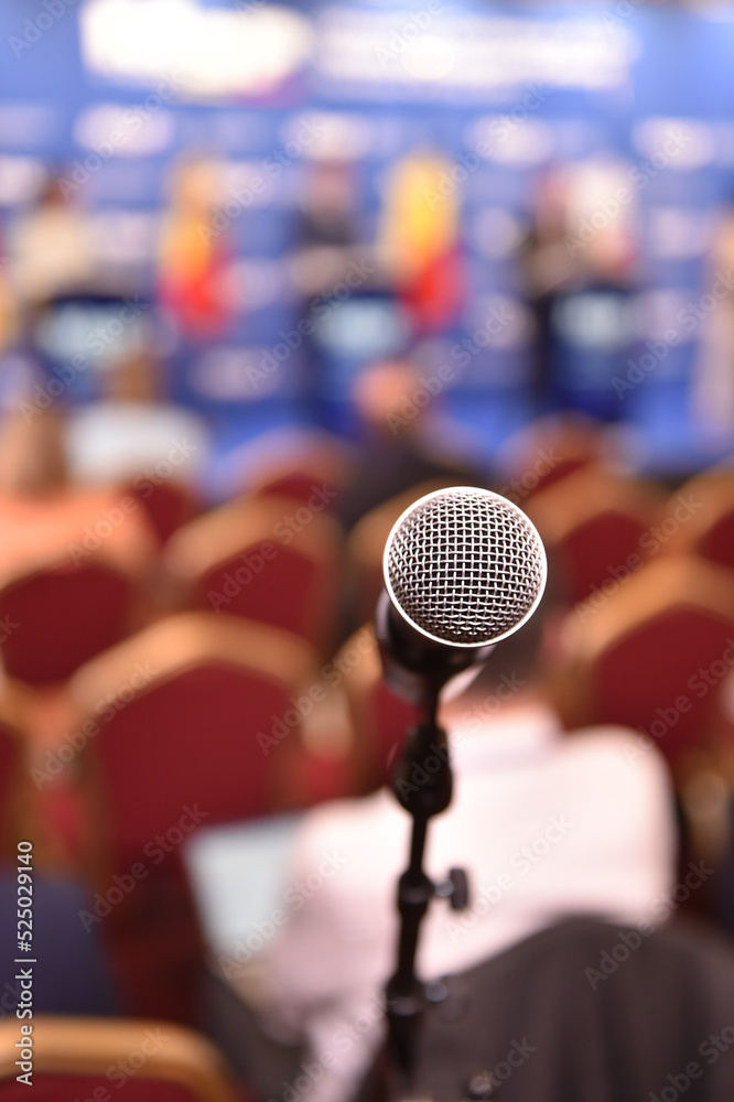 Detail shot with a microphone during a press conference. Audience in the background Detail shot with a microphone during a press conference. Audience in the background