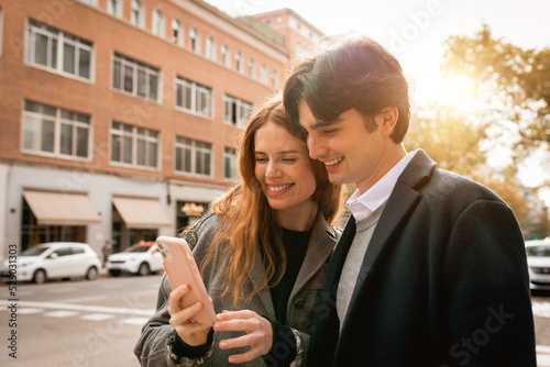 Loving young couple standing using smartphone on street