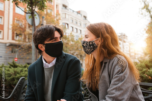 Young couple in masks resting on bench