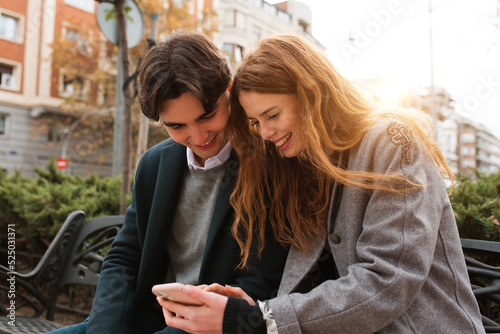 Cheerful couple browsing smartphone on city street