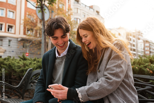 Cheerful couple browsing smartphone on city street