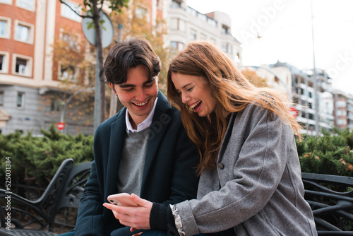 Cheerful couple browsing smartphone on city street