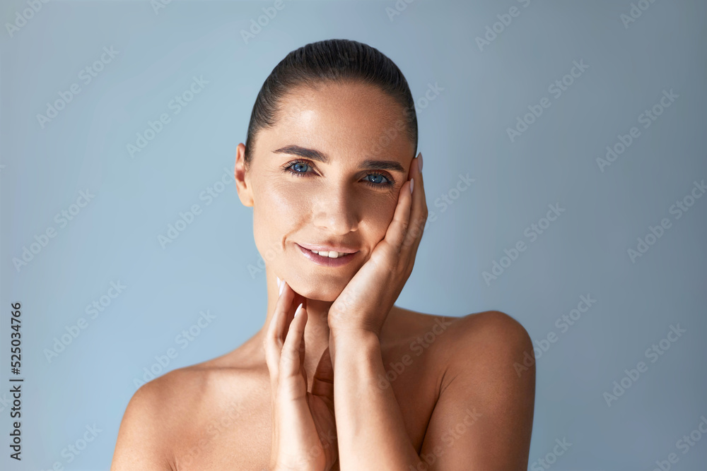Facial anti age care. Beauty portrait of mature attractive  woman touching her face against grey background